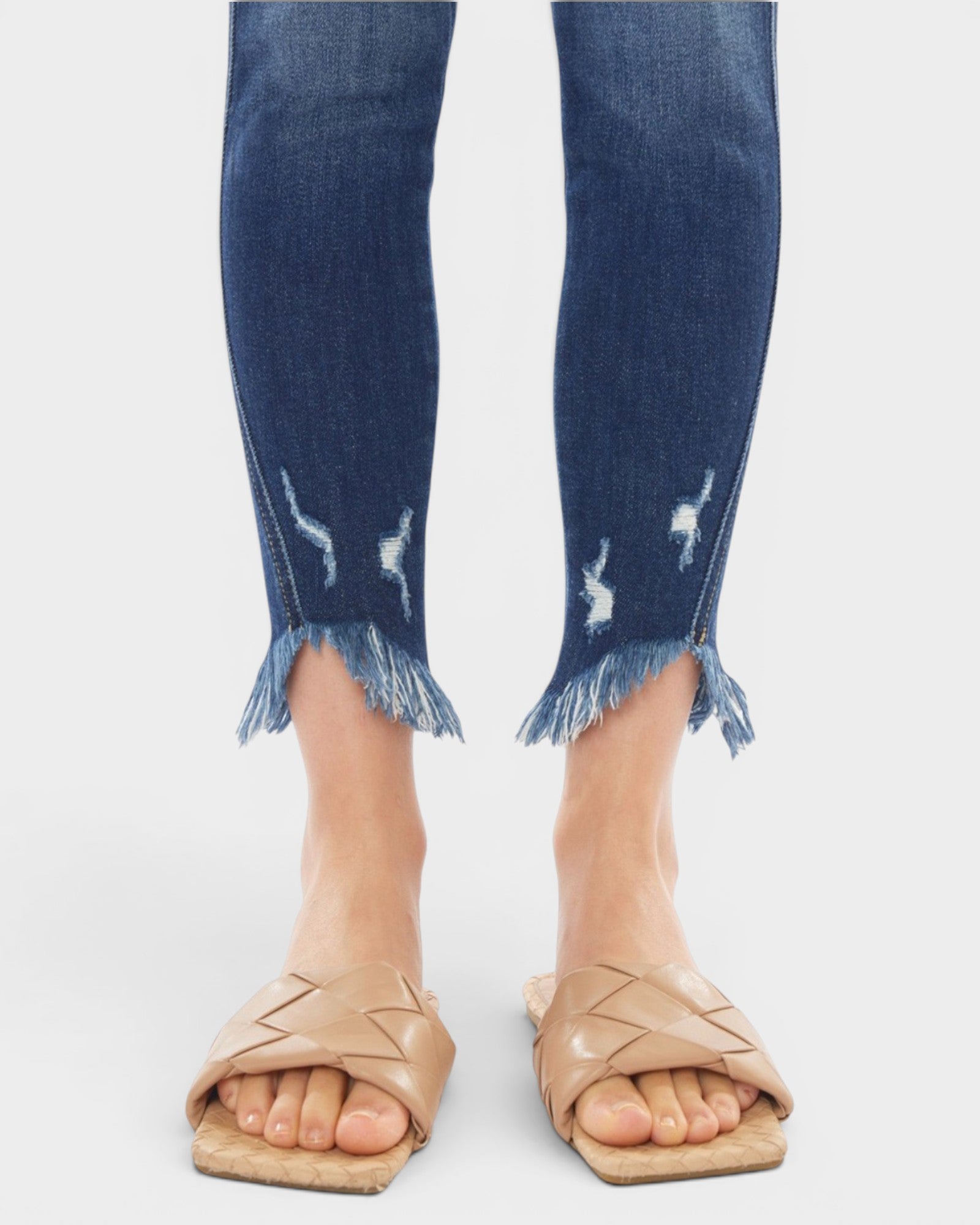 Blue jeans with frayed cuffs worn by a person on a white background