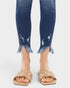 Blue jeans with frayed cuffs worn by a person on a white background