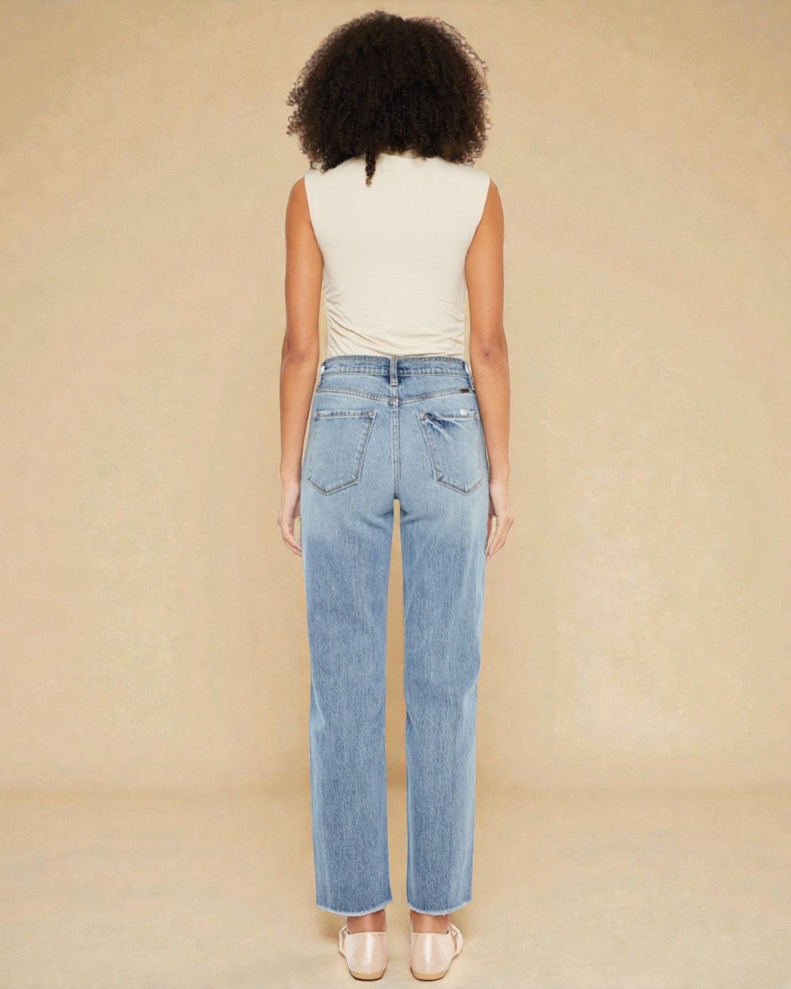 Person wearing light blue jeans and a white top on a beige background