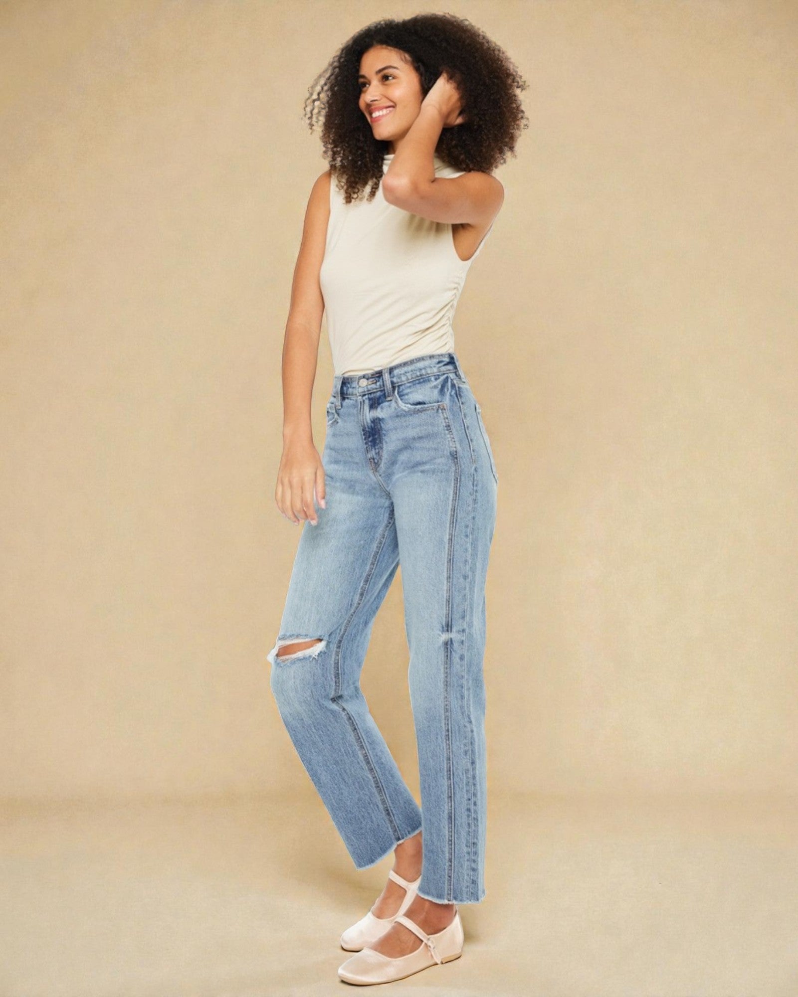 Woman wearing light blue jeans and a white top on a beige background