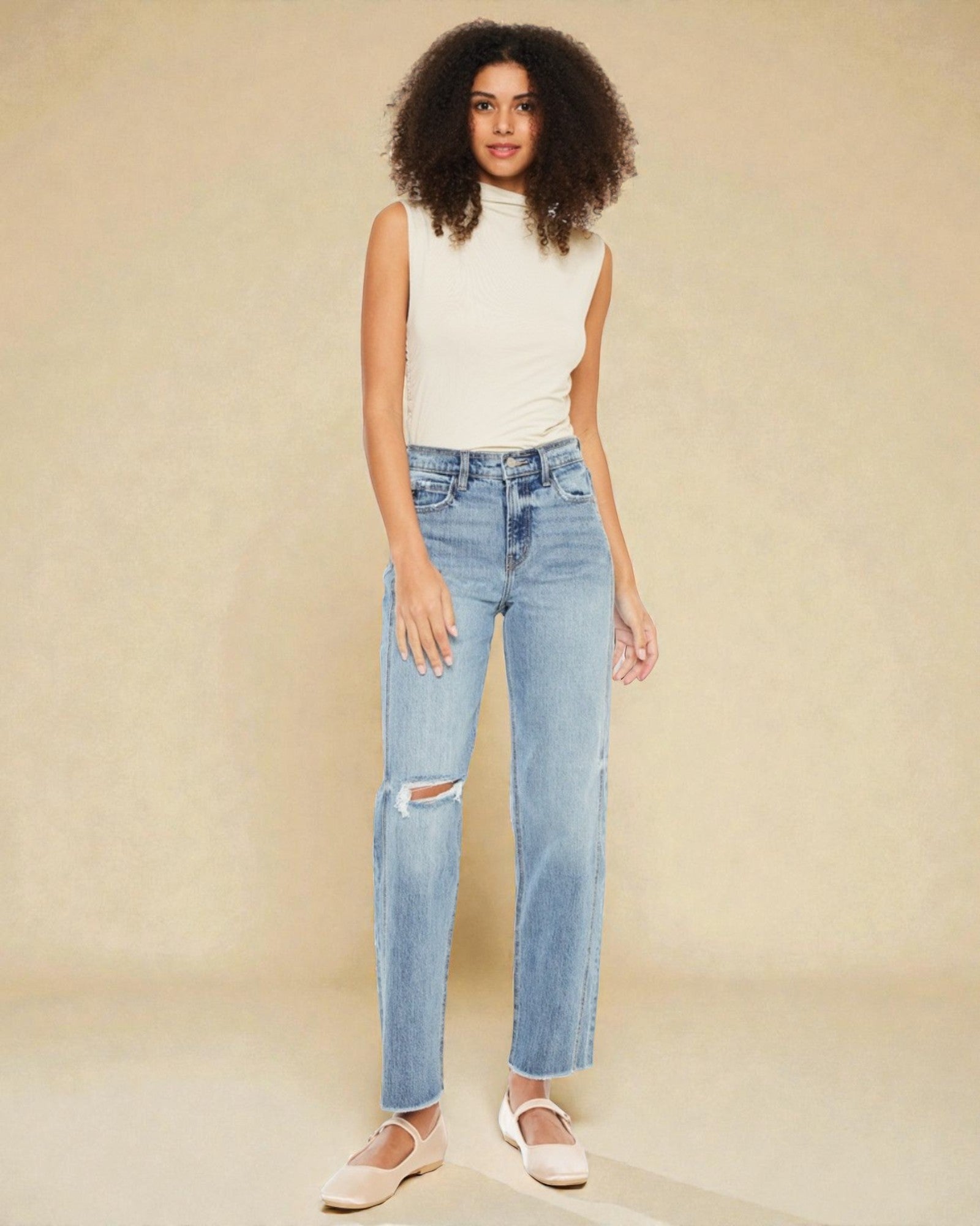 Woman wearing light blue jeans with a distressed knee on a beige background