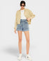 Person wearing a beige jacket, white shirt, denim shorts, and white sneakers on a white background