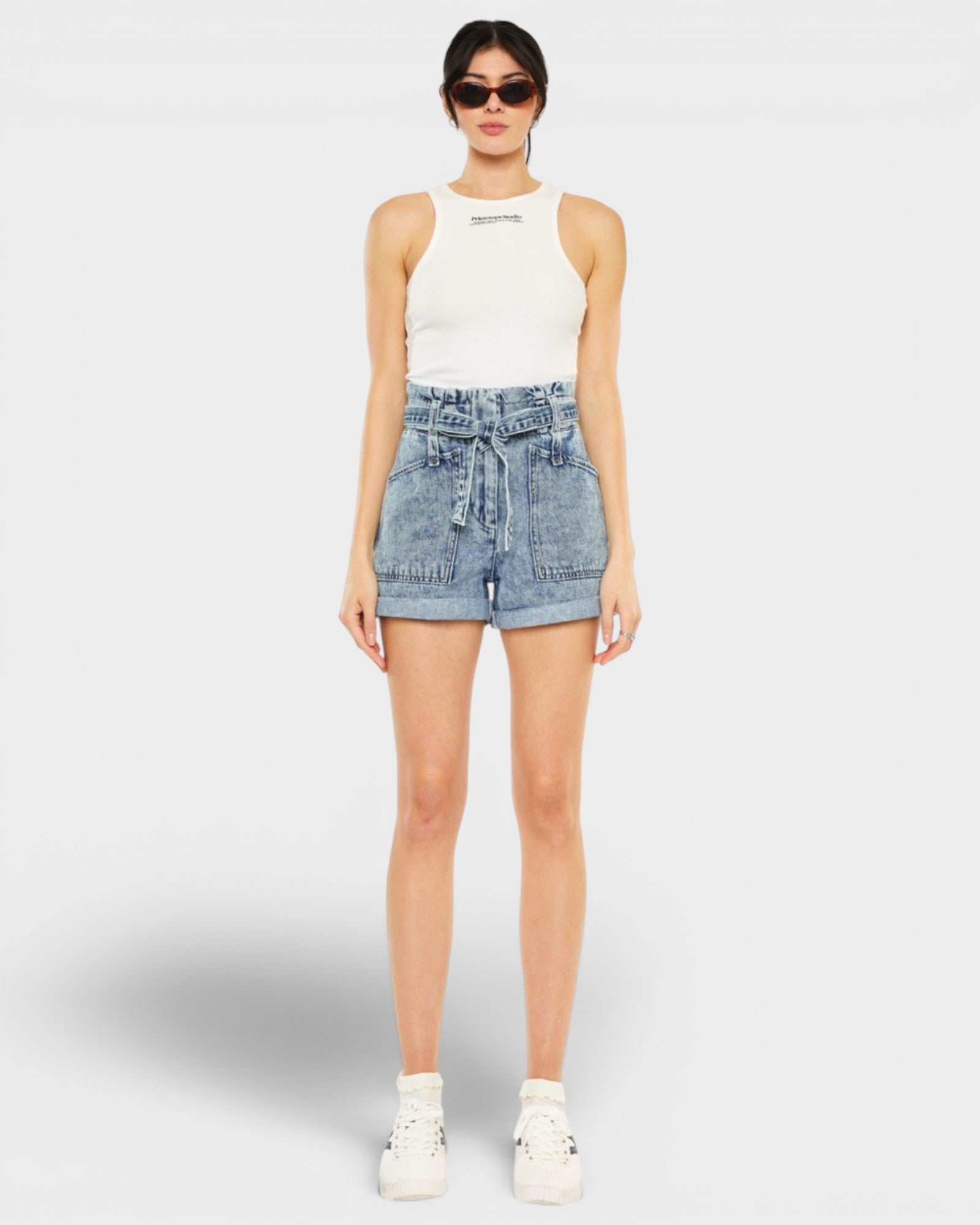 Woman wearing a white sleeveless top and denim shorts on a white background