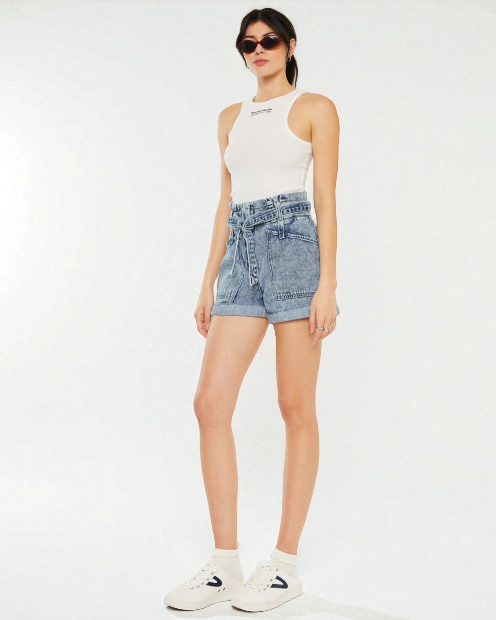 Woman wearing a white tank top and denim shorts on a white background