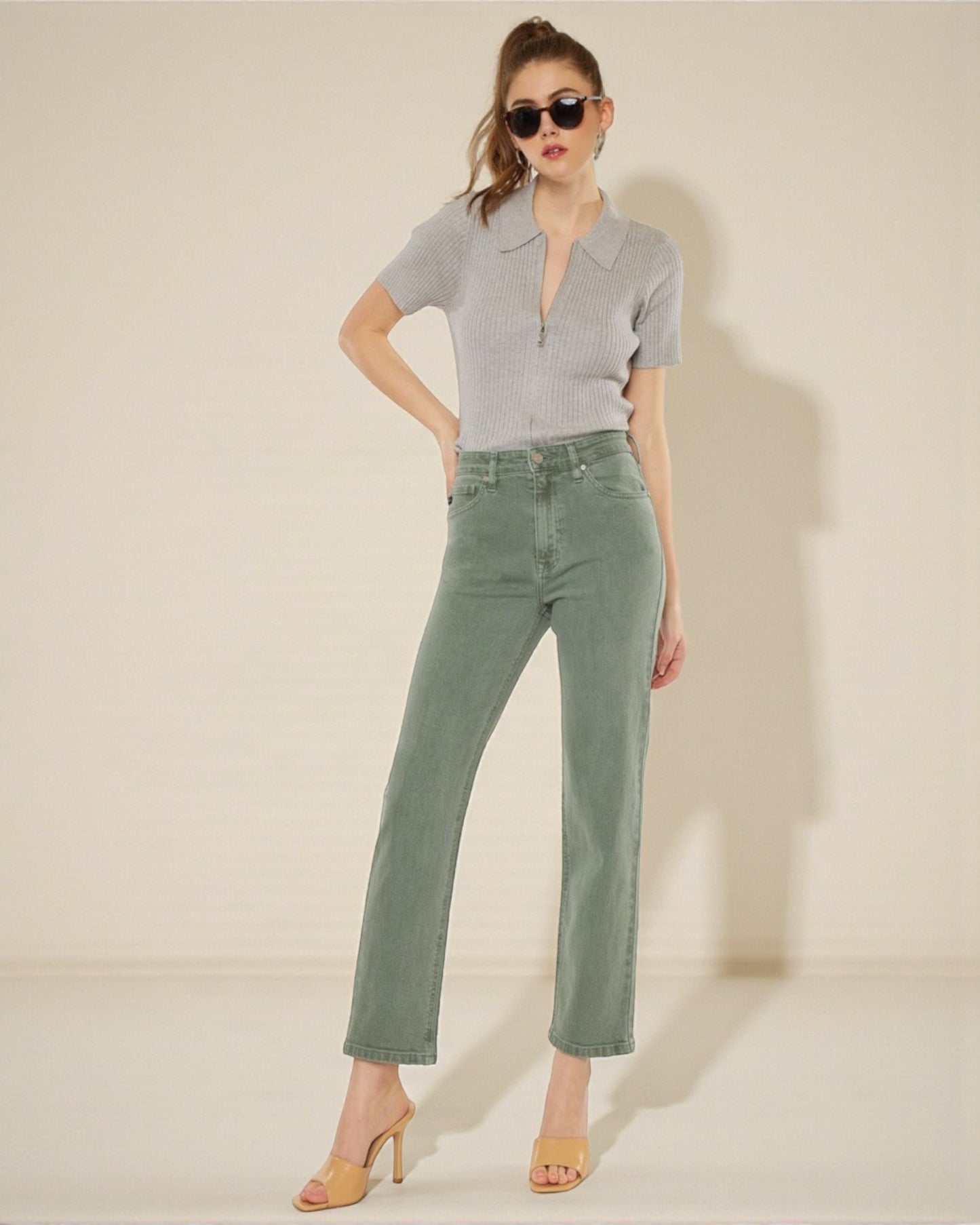 Woman wearing a gray polo shirt and green jeans against a plain background