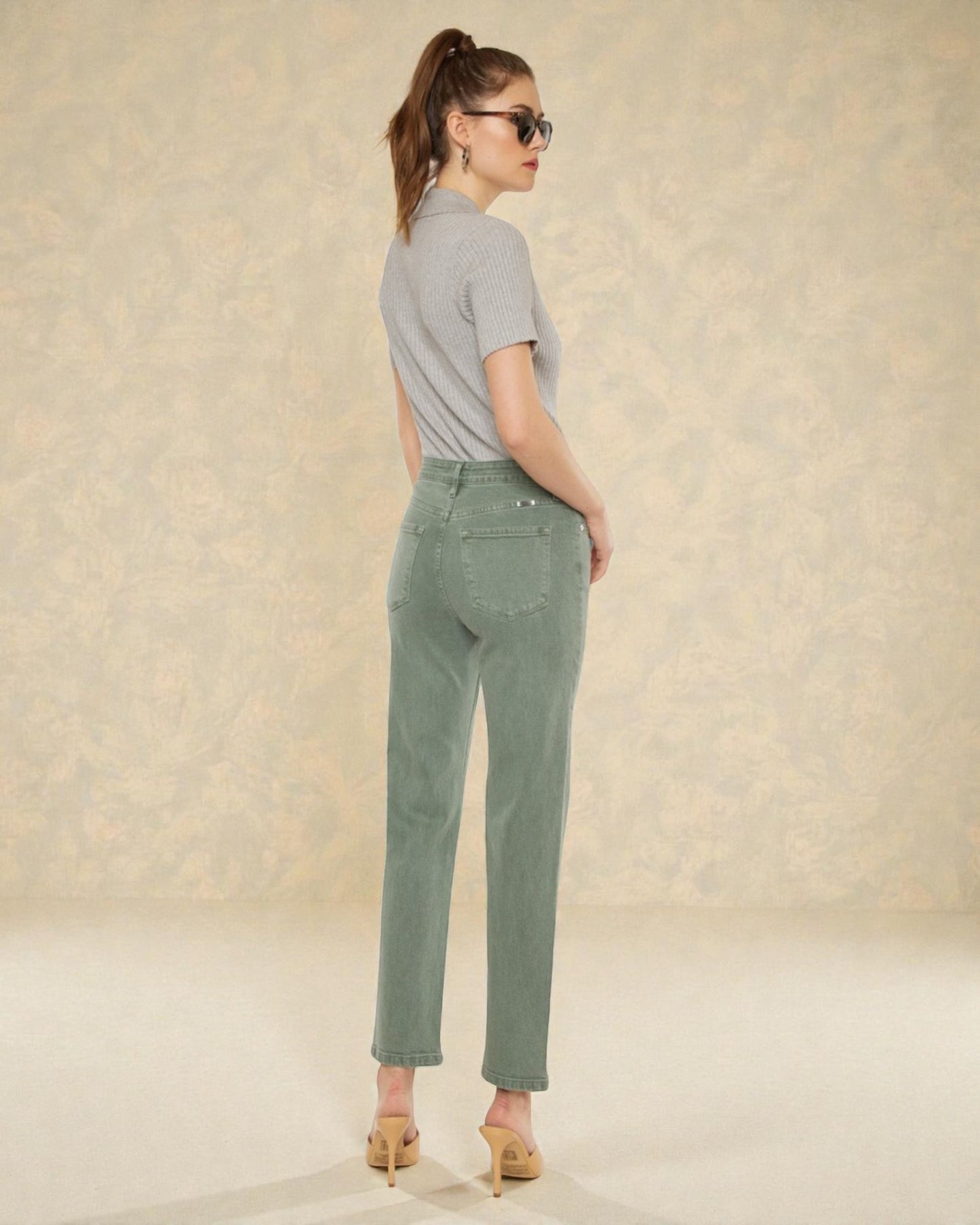 Woman wearing a gray shirt and green pants against a beige background