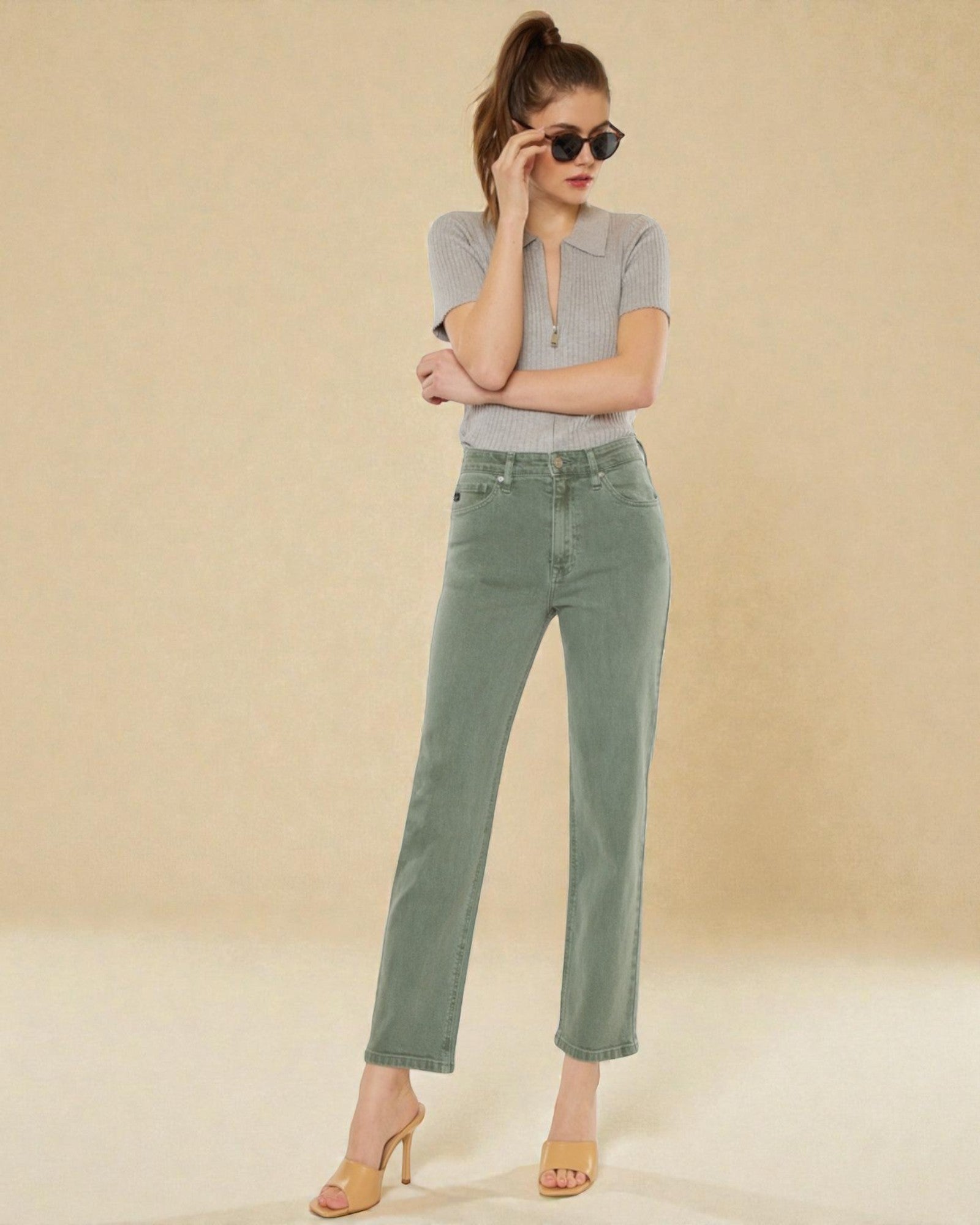 Woman wearing a gray top and green jeans against a beige background