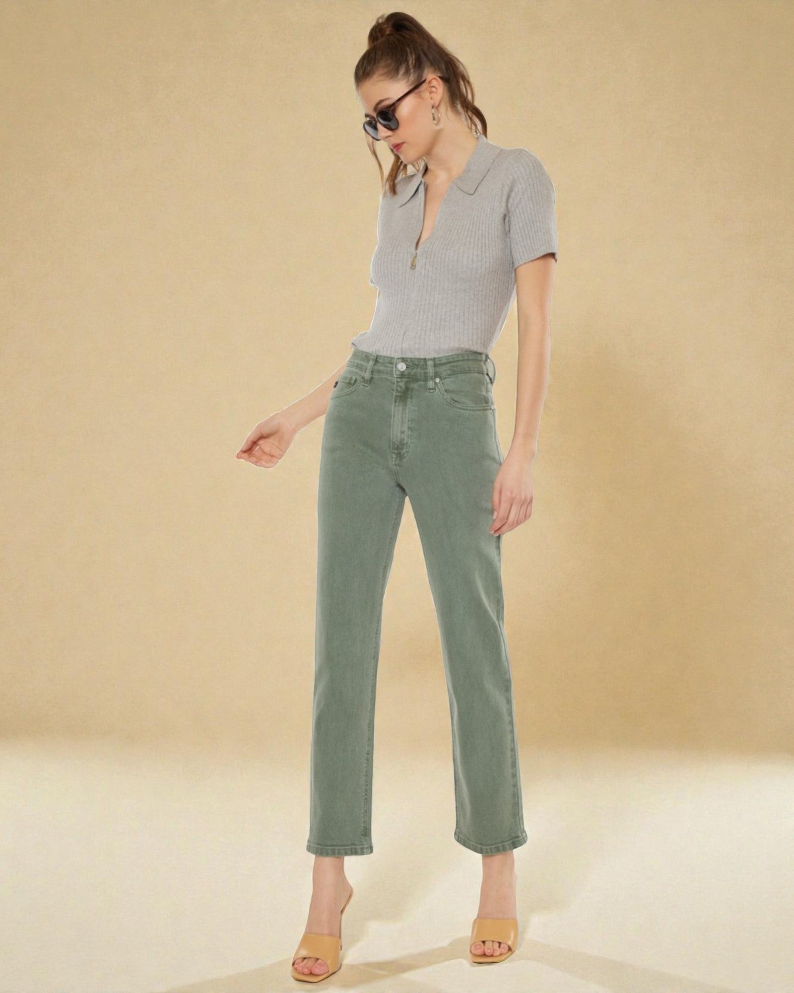 Woman wearing a gray polo shirt and green jeans on a beige background
