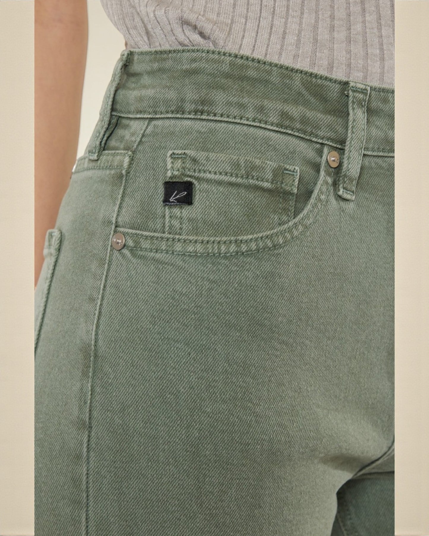 Green jeans with a brand logo on the pocket against a beige background