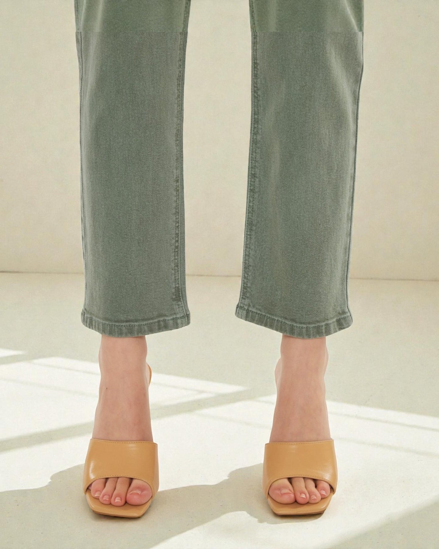 Person wearing tan open-toe sandals with rolled-up green jeans on a light background