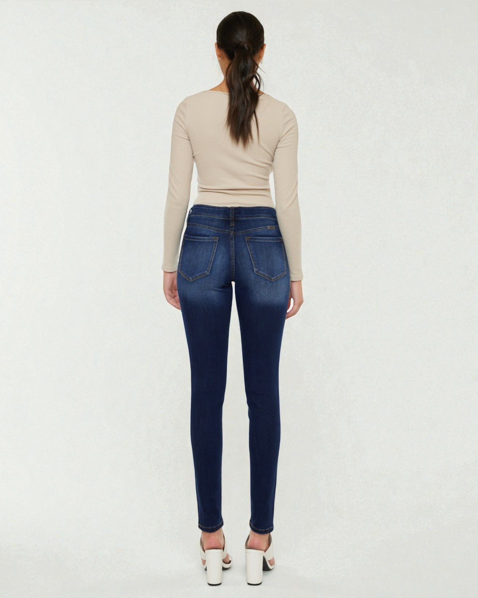 Person wearing blue jeans and a beige top on a white background