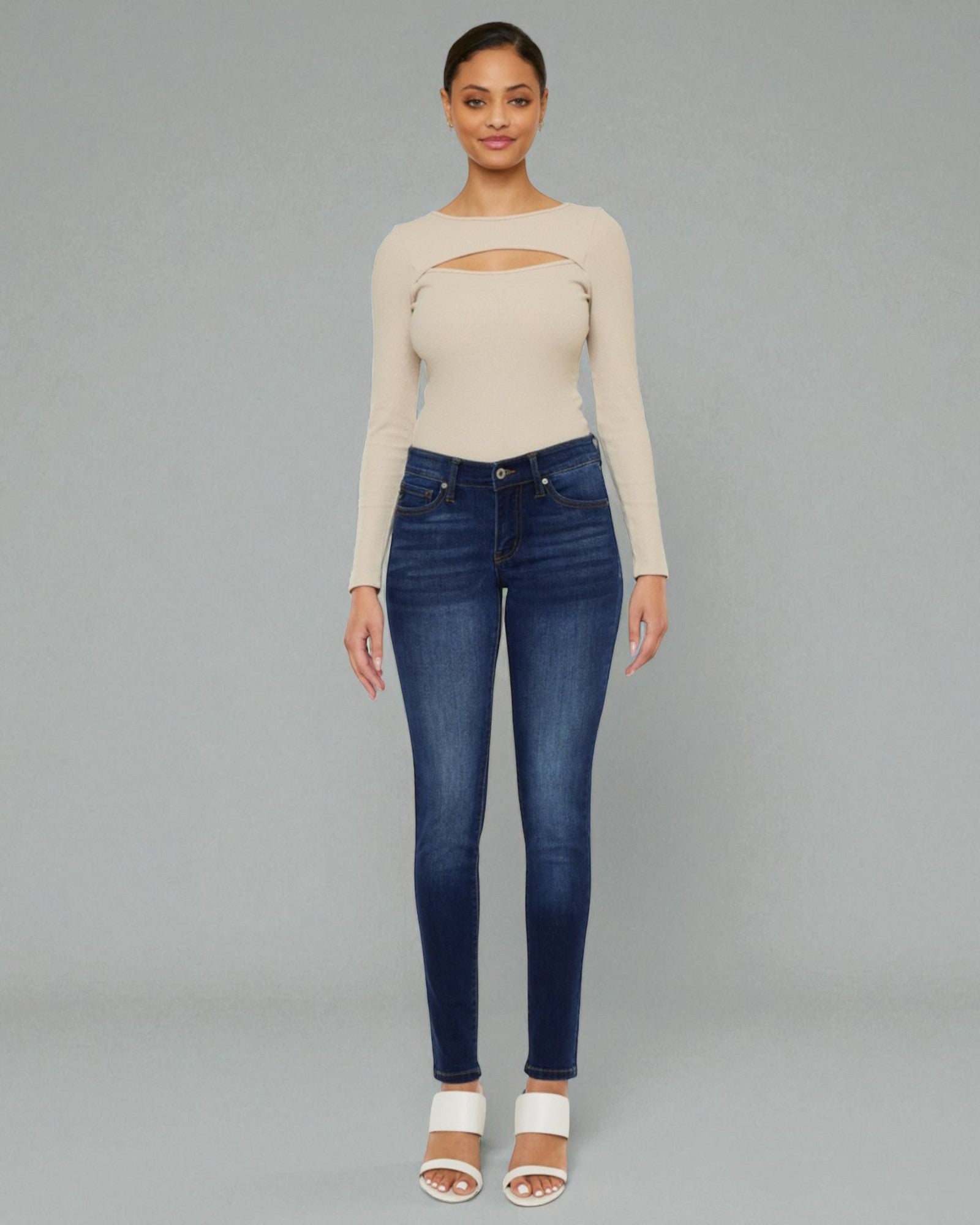 Woman wearing a beige long-sleeve top and blue jeans on a gray background