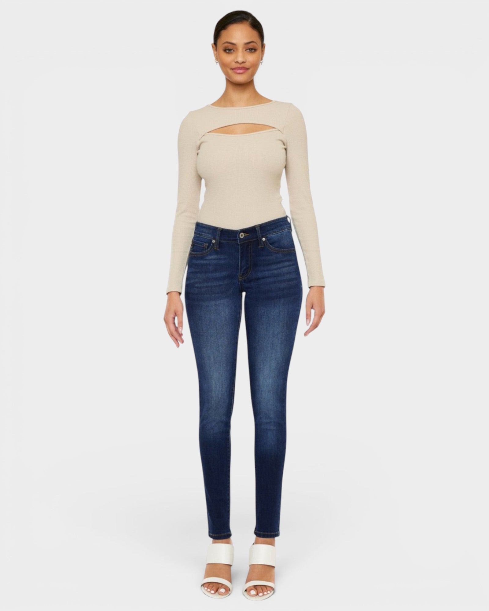 Woman wearing a beige long-sleeve top and blue jeans on a white background