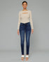Woman wearing a beige long-sleeve top and blue jeans on a gray background