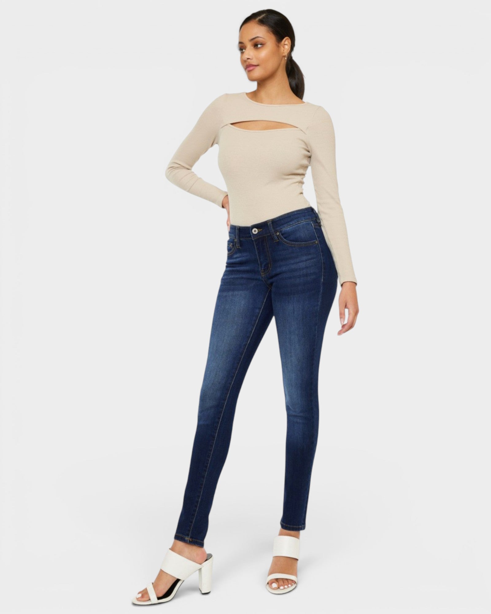 Woman wearing a beige long-sleeve top and blue jeans on a white background