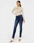 Woman wearing a beige long-sleeve top and blue jeans on a white background