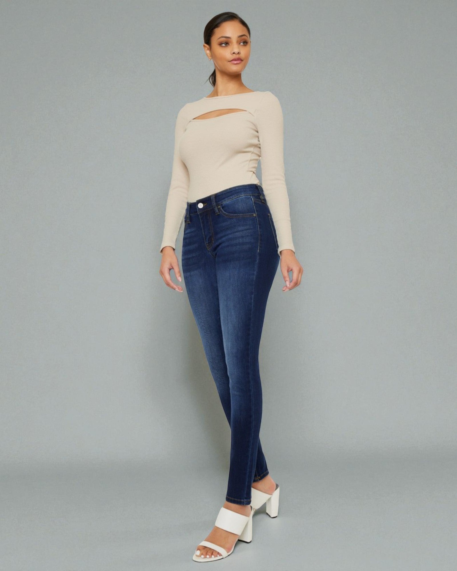 Woman wearing a beige sweater and blue jeans on a gray background