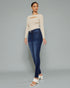 Woman wearing a beige sweater and blue jeans on a gray background