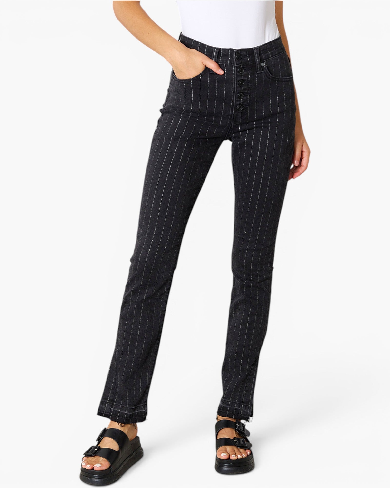 A model wearing black pinstriped ankle-length jeans with a white top and black sandals, shown from the waist down on a light gray background.