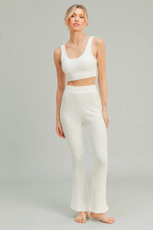 Woman wearing a white tank top and pants on a gray background