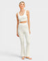 Woman wearing a white tank top and pants on a light gray background