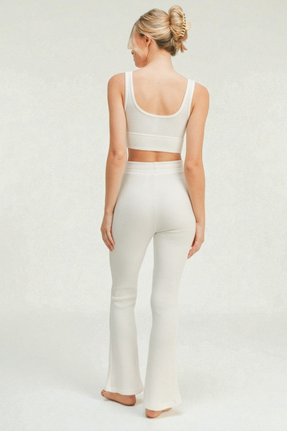 Woman wearing a white tank top and flared pants on a plain background