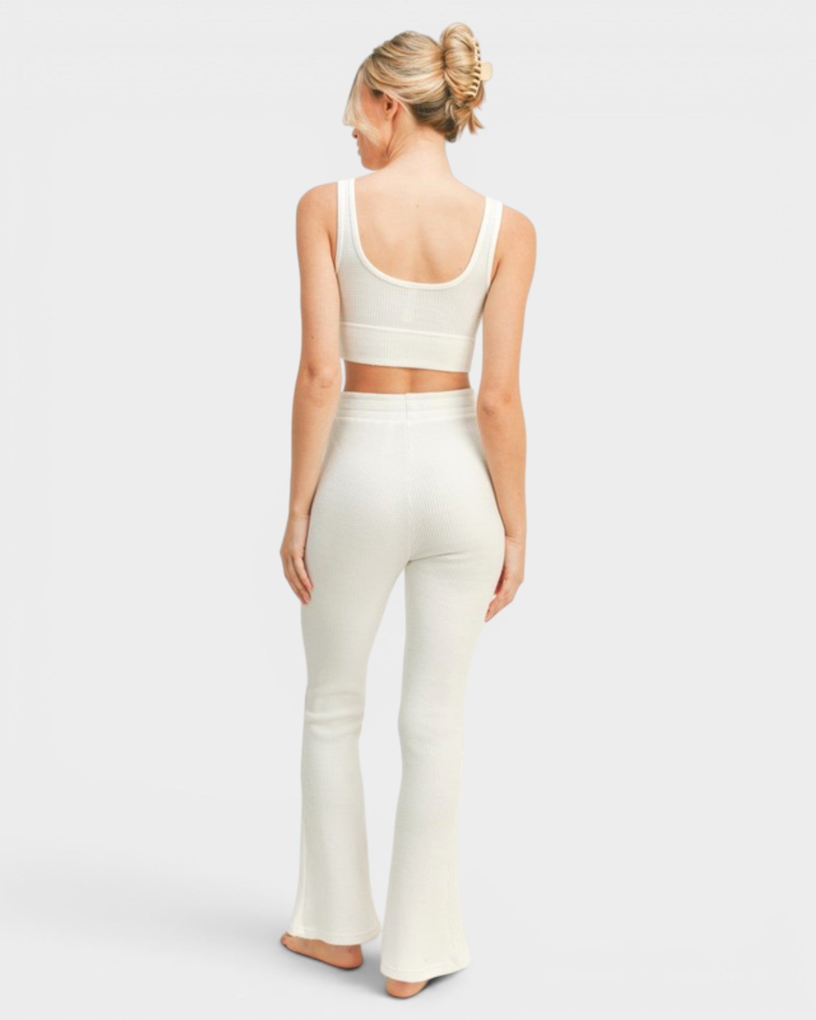 Woman wearing a white sleeveless top and flared pants on a light gray background