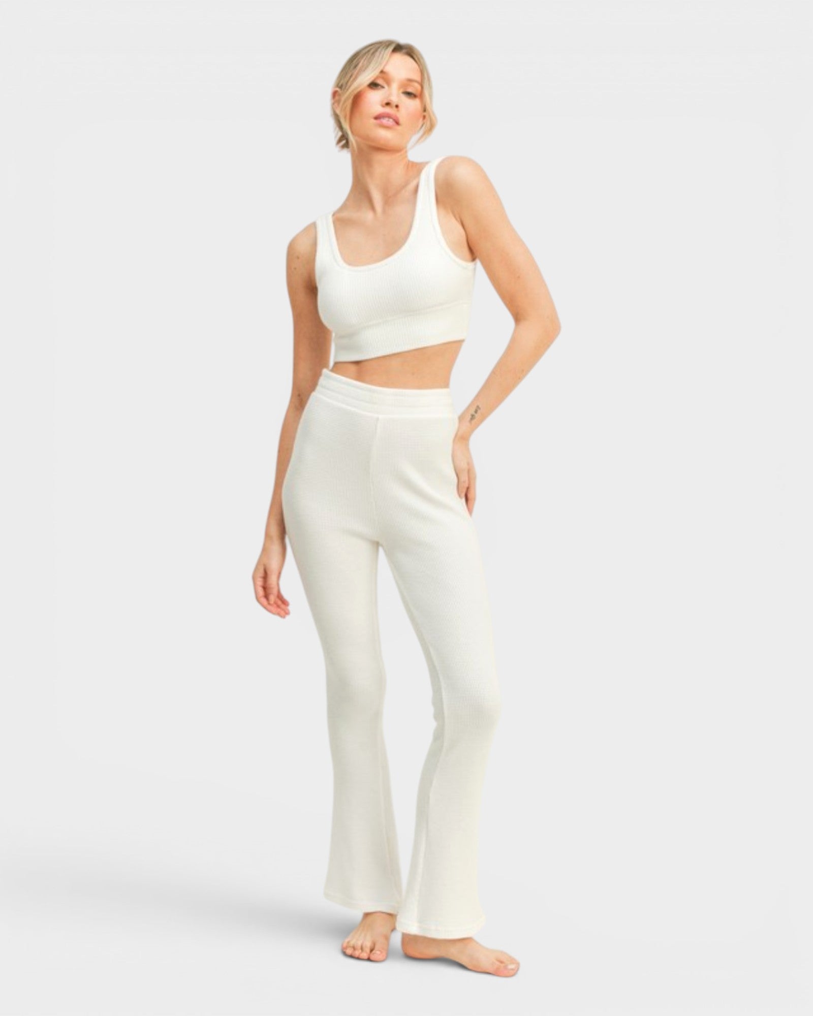 Woman wearing a white sports bra and leggings on a light gray background