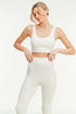 Woman wearing a white sports bra and leggings on a plain background