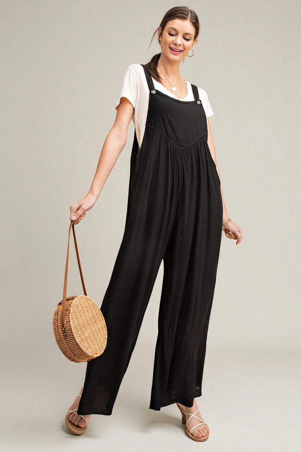 Woman wearing a black jumpsuit holding a woven bag on a plain background