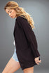 Woman wearing a black jacket over a white top and denim shorts on a gray background