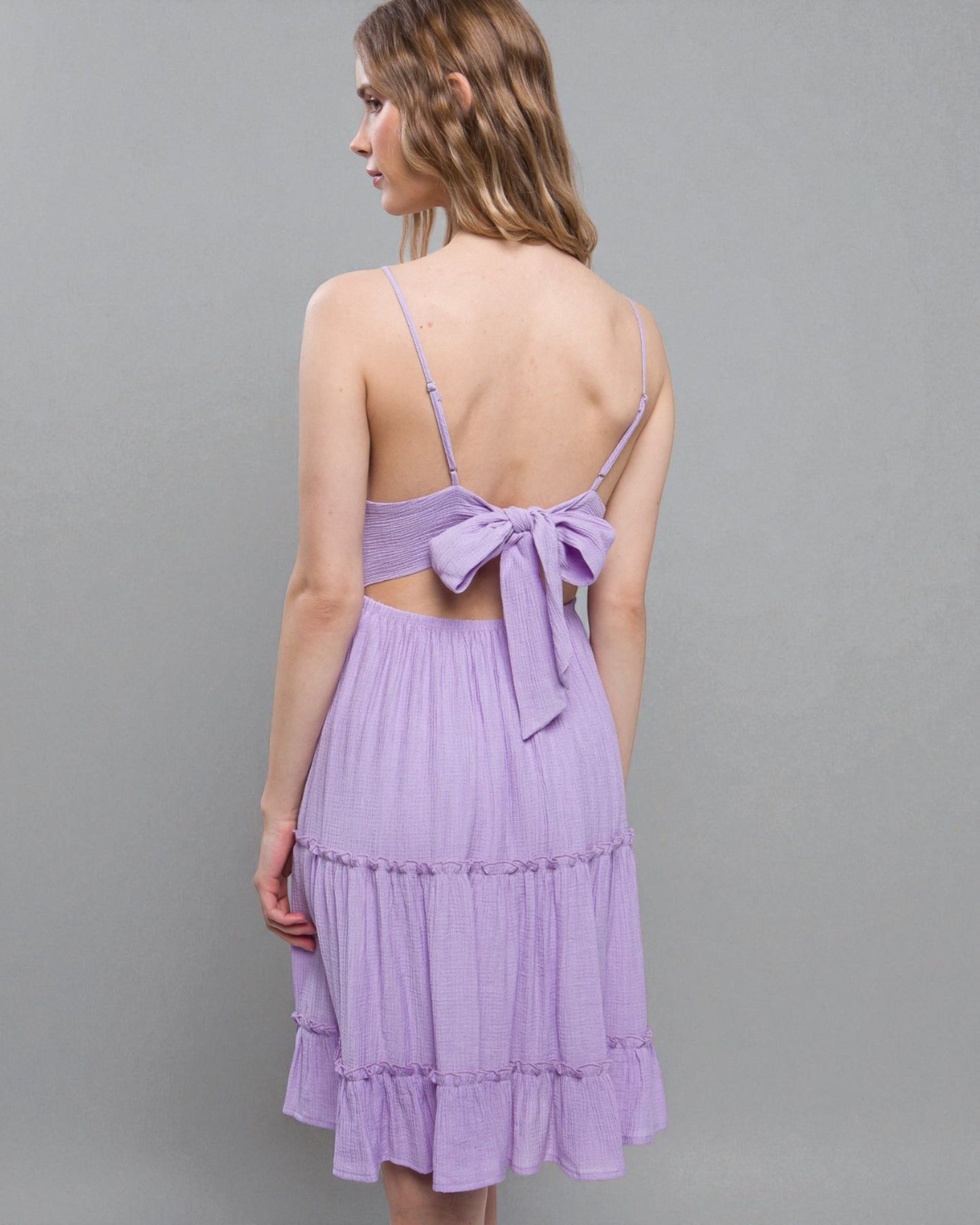 Woman wearing a purple dress with a bow detail on a gray background