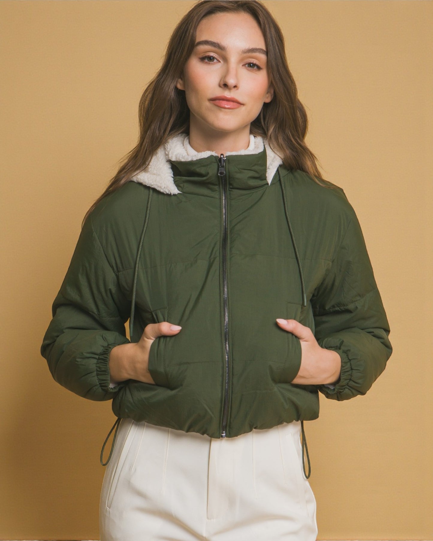 Woman wearing a green puffer jacket with a beige background