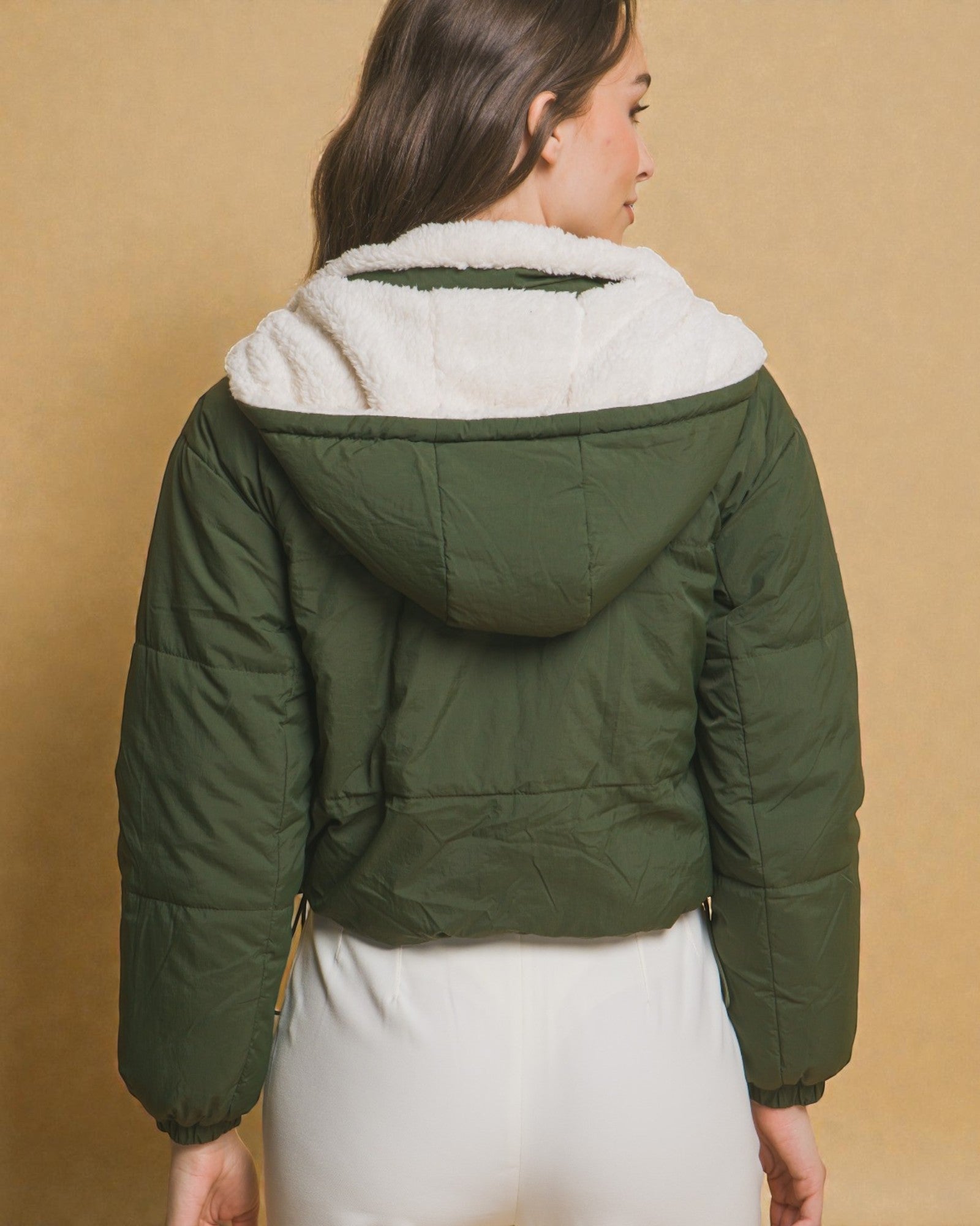Green puffer jacket with white fur lining worn by a person on a beige background