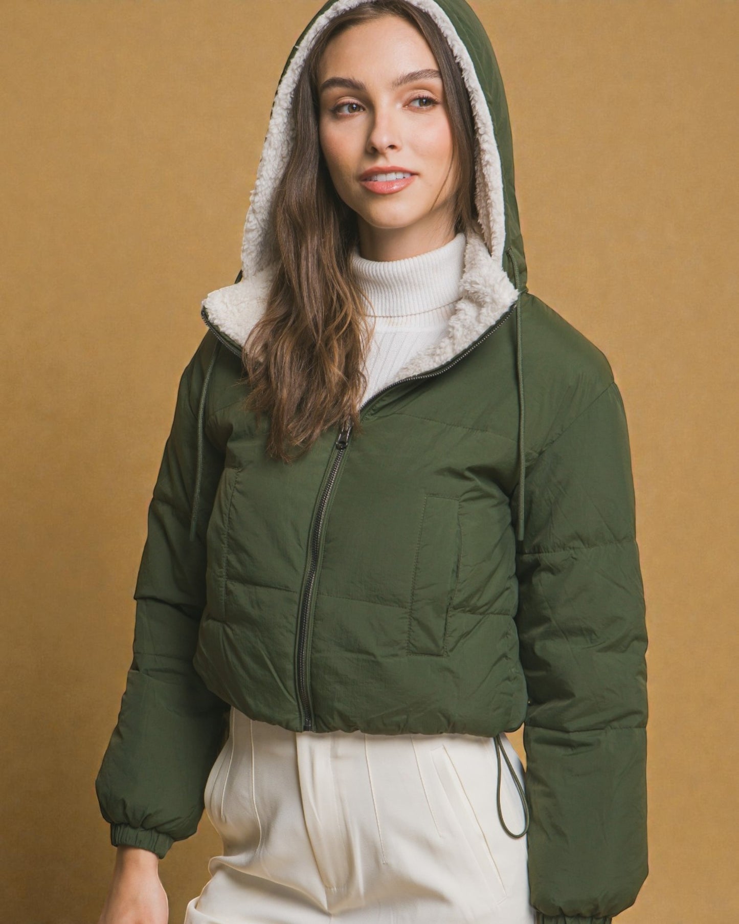 Woman wearing a green puffer jacket with a hood against a beige background