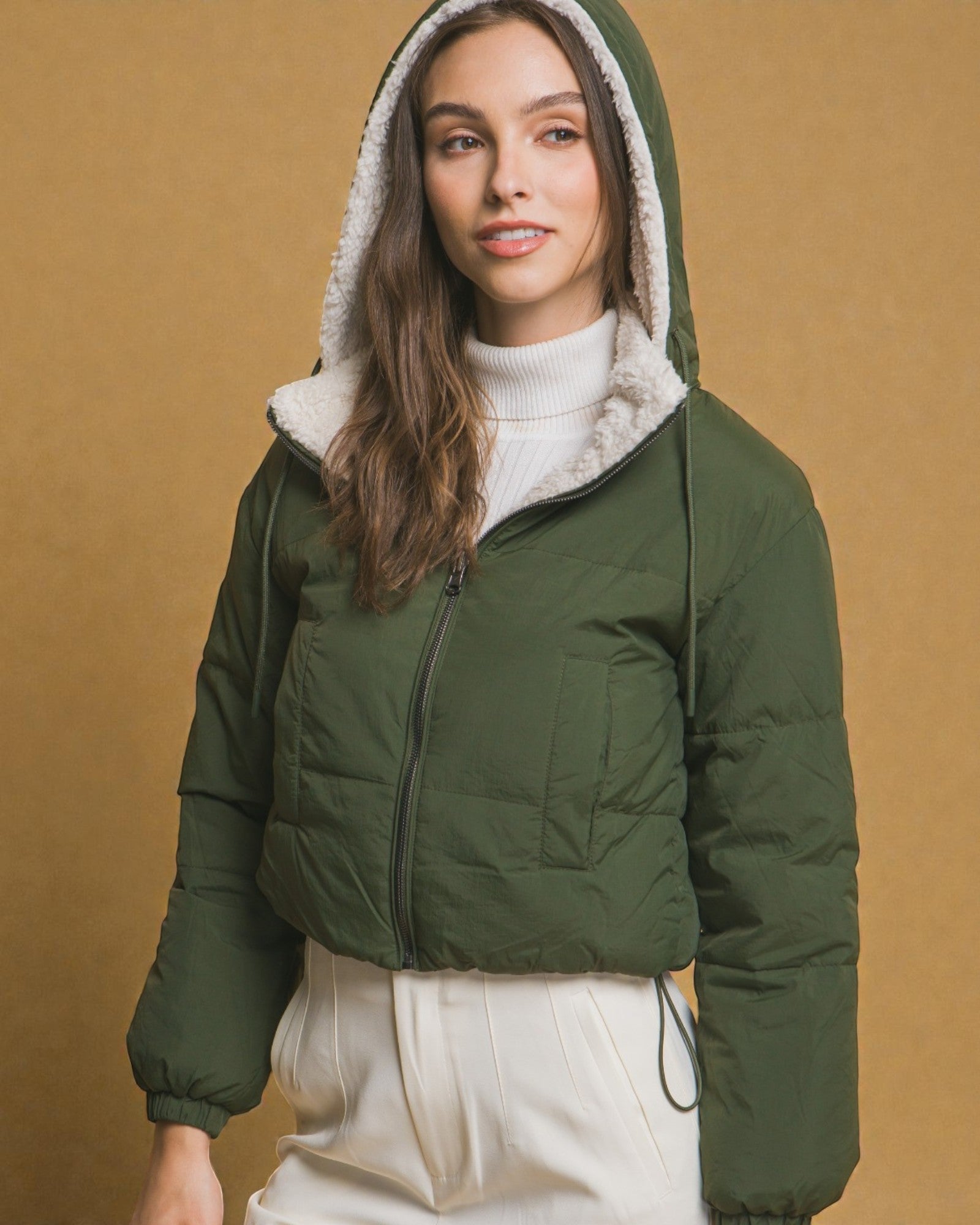 Woman wearing a green puffer jacket with a hood against a beige background