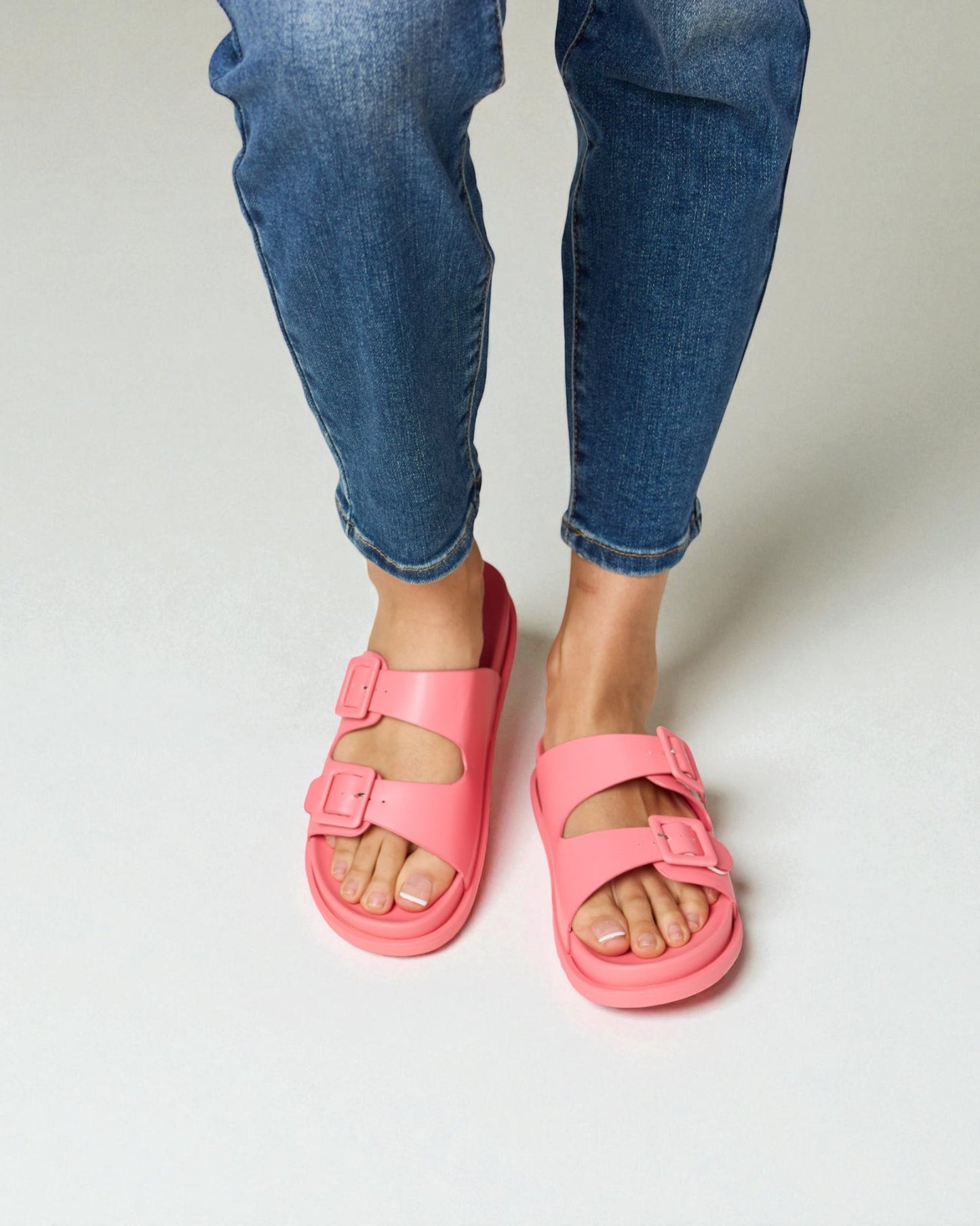 Person wearing bright pink sandals and blue jeans on a plain background