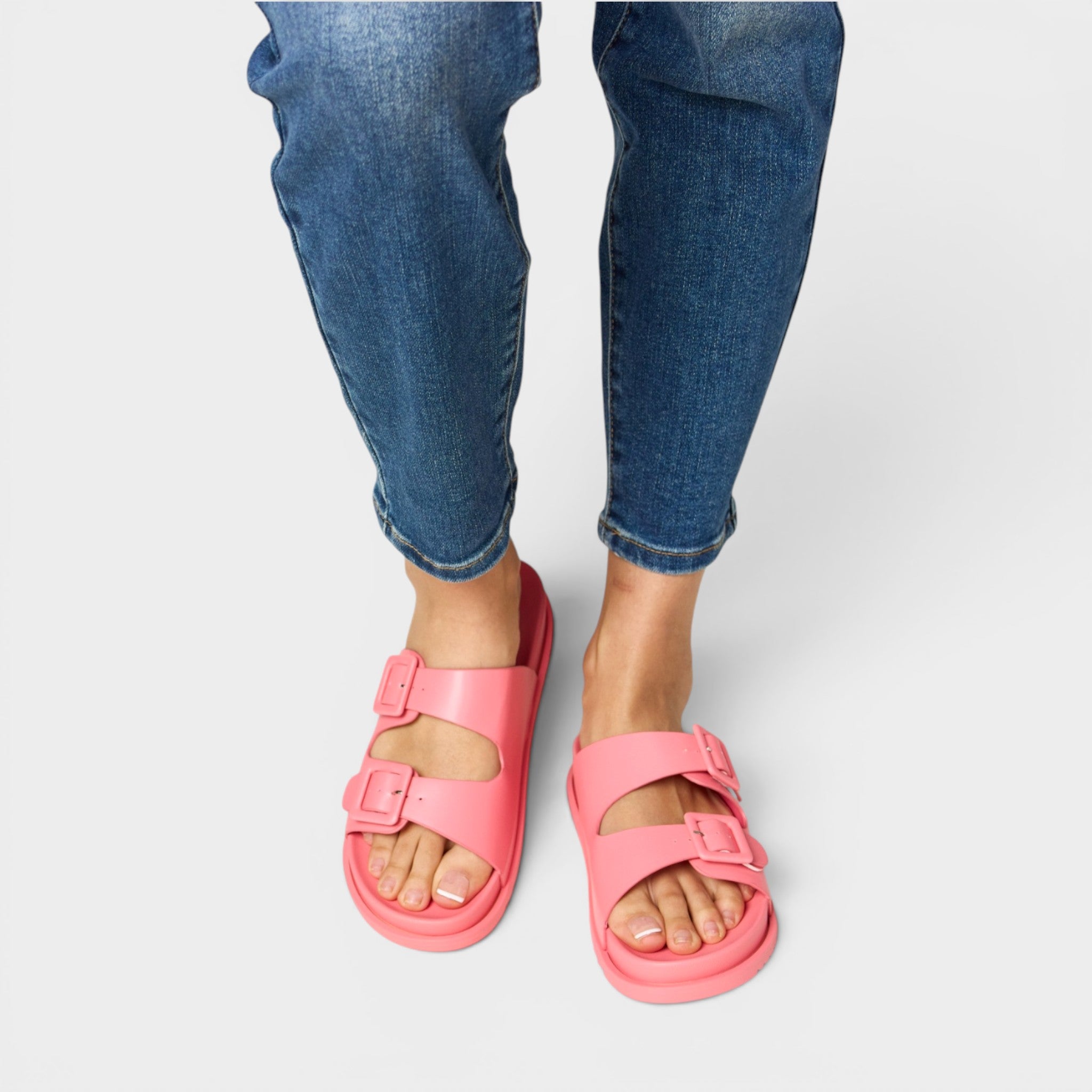 Pink sandals worn with blue jeans on a light gray background