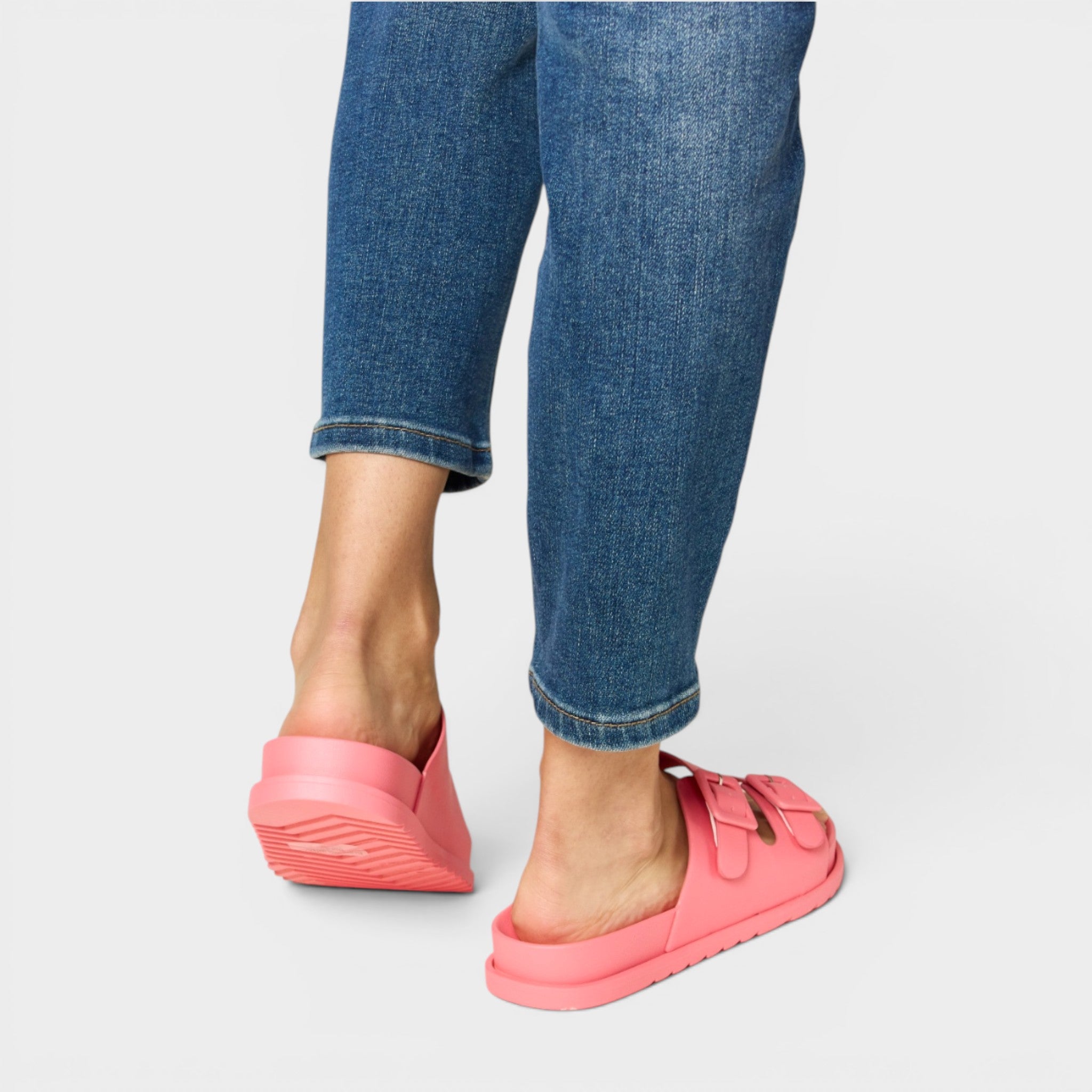 Person wearing pink slip-on shoes with blue jeans on a light gray background