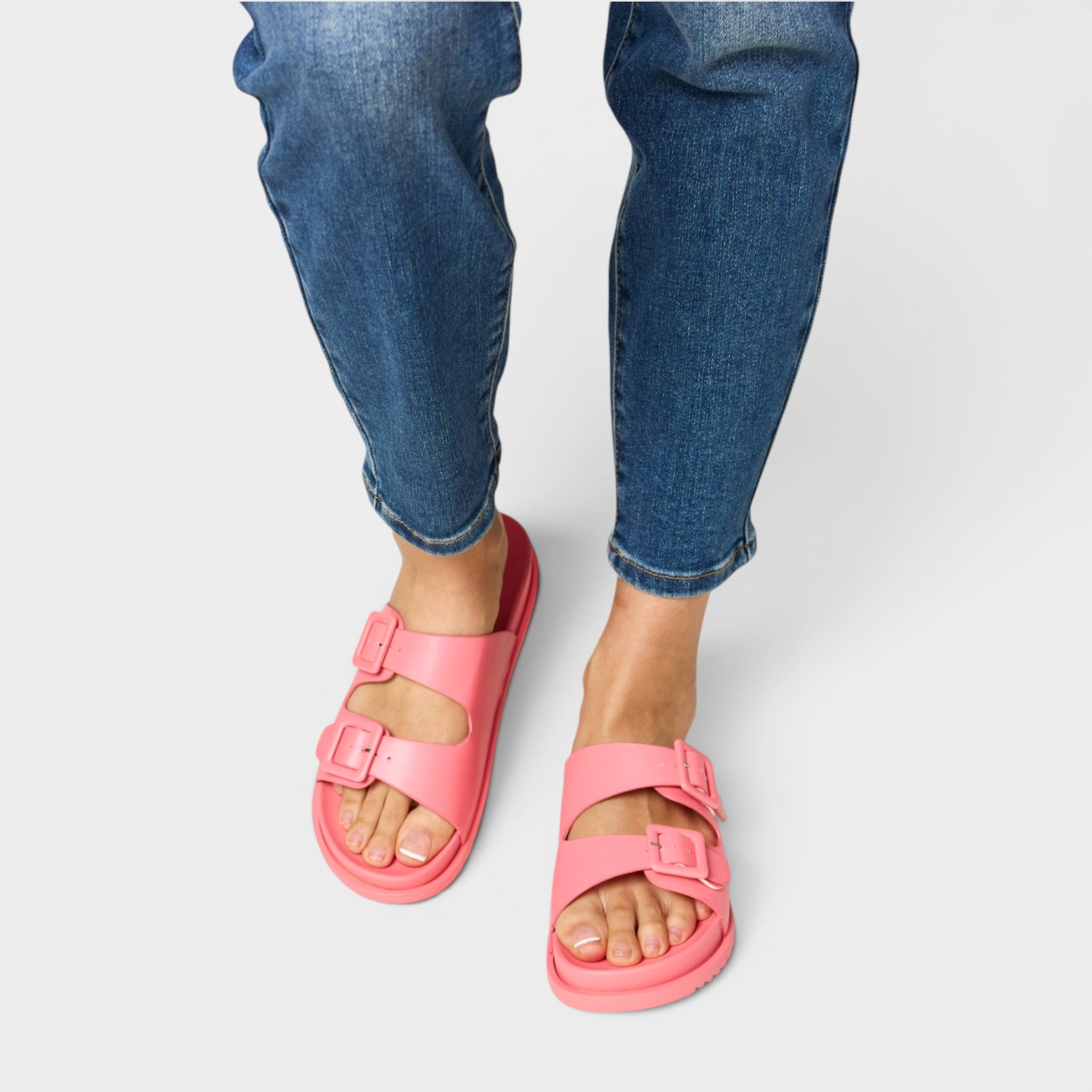 Pink sandals worn with blue jeans on a white background