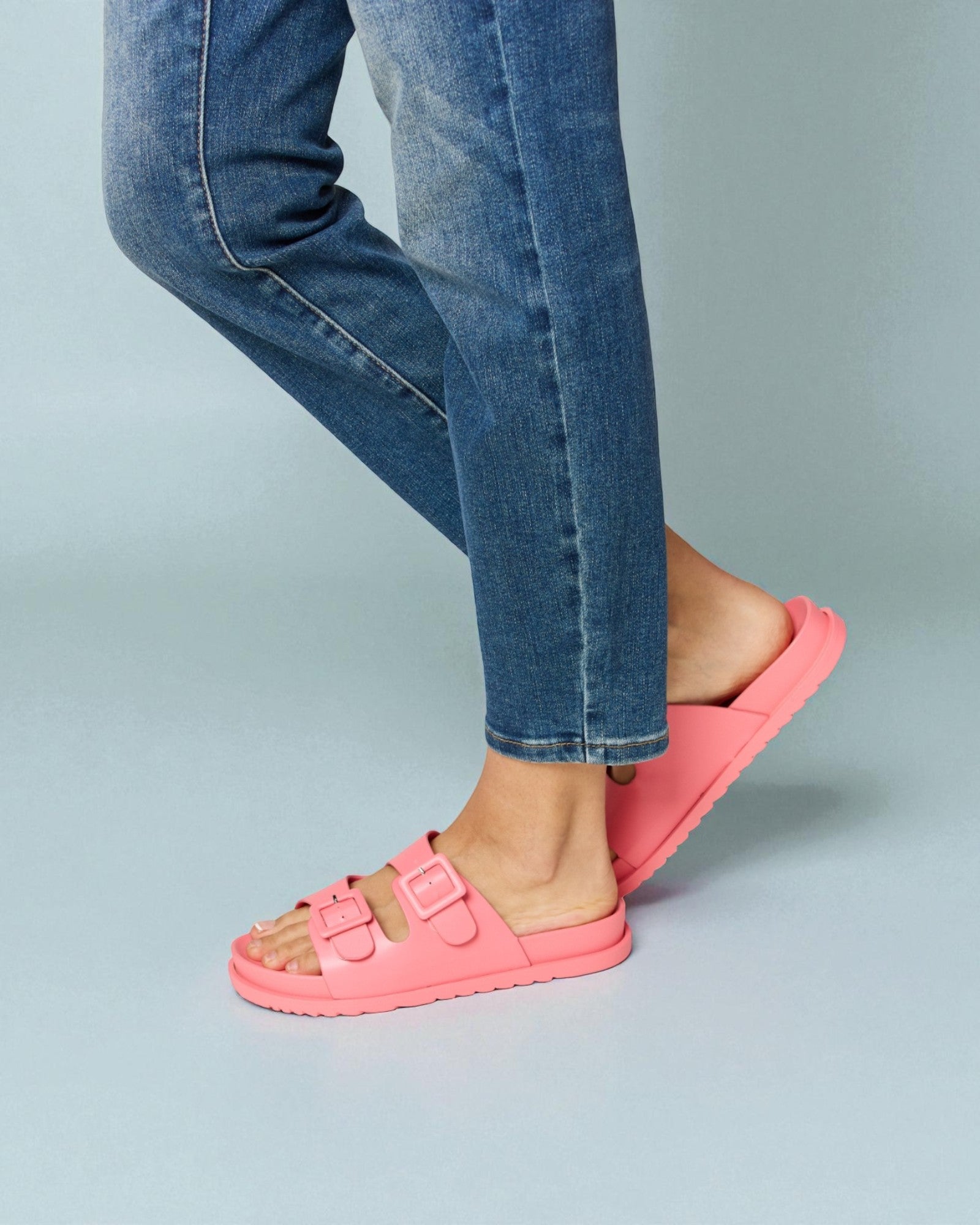 Person wearing blue jeans and pink sandals on a gray background