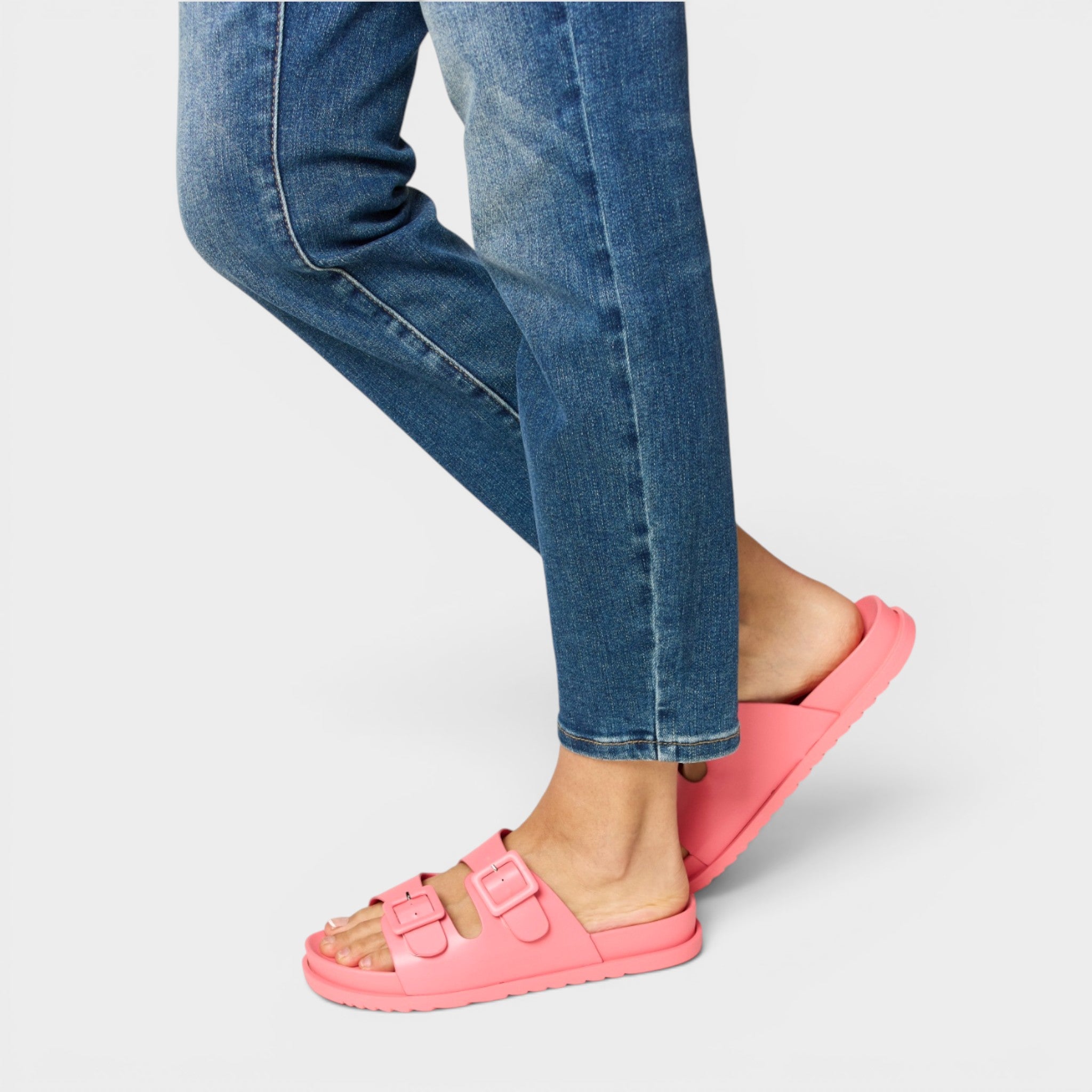 Person wearing blue jeans and pink sandals on a light gray background