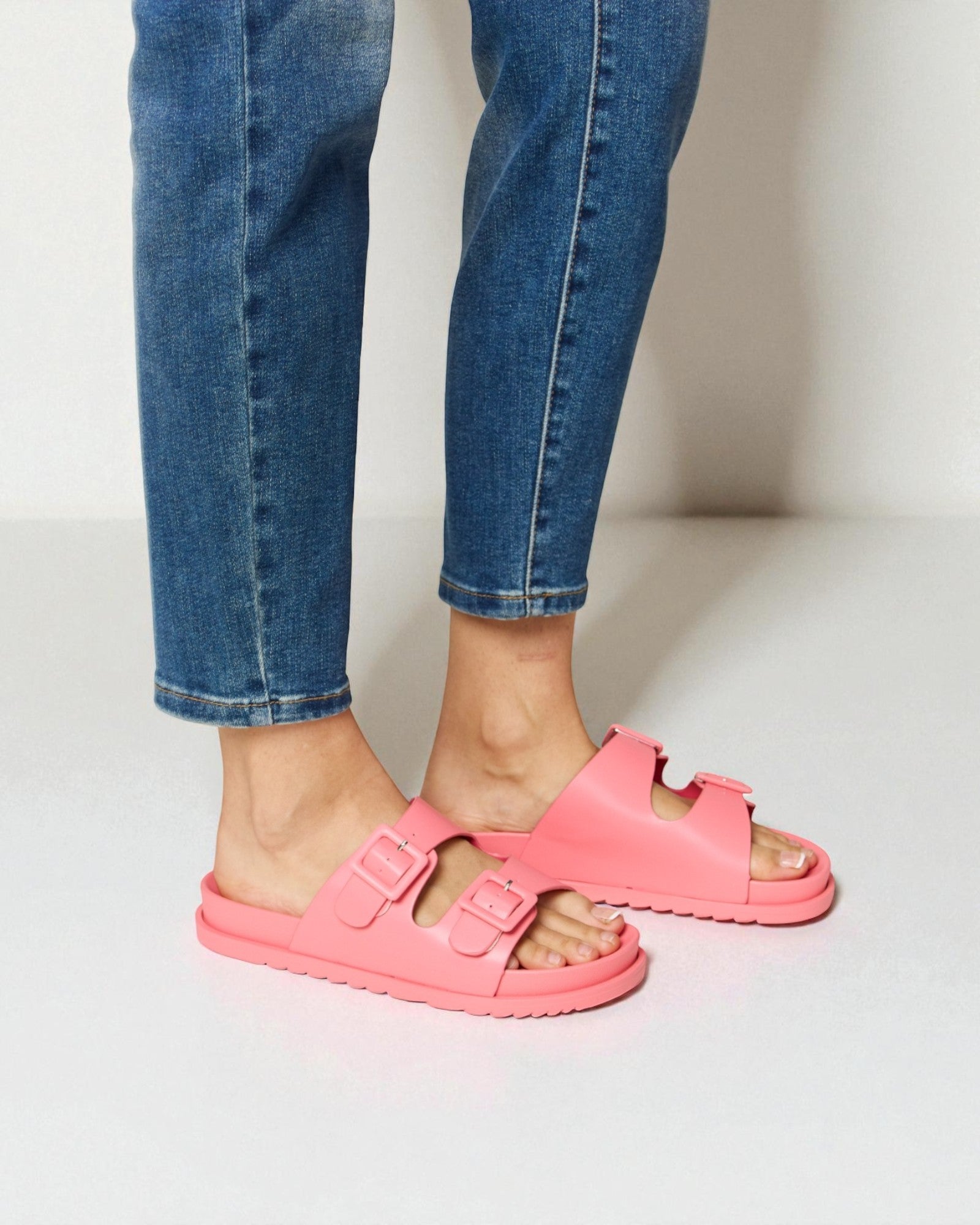 Person wearing bright pink sandals with blue jeans on a light background