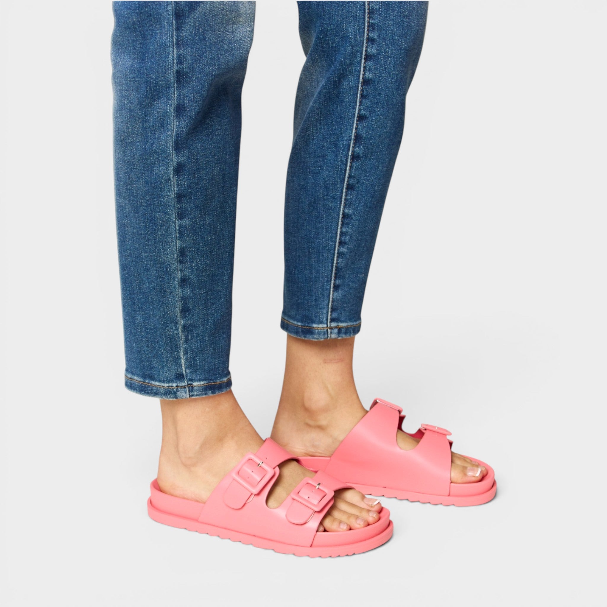 Person wearing pink sandals with blue jeans on a white background