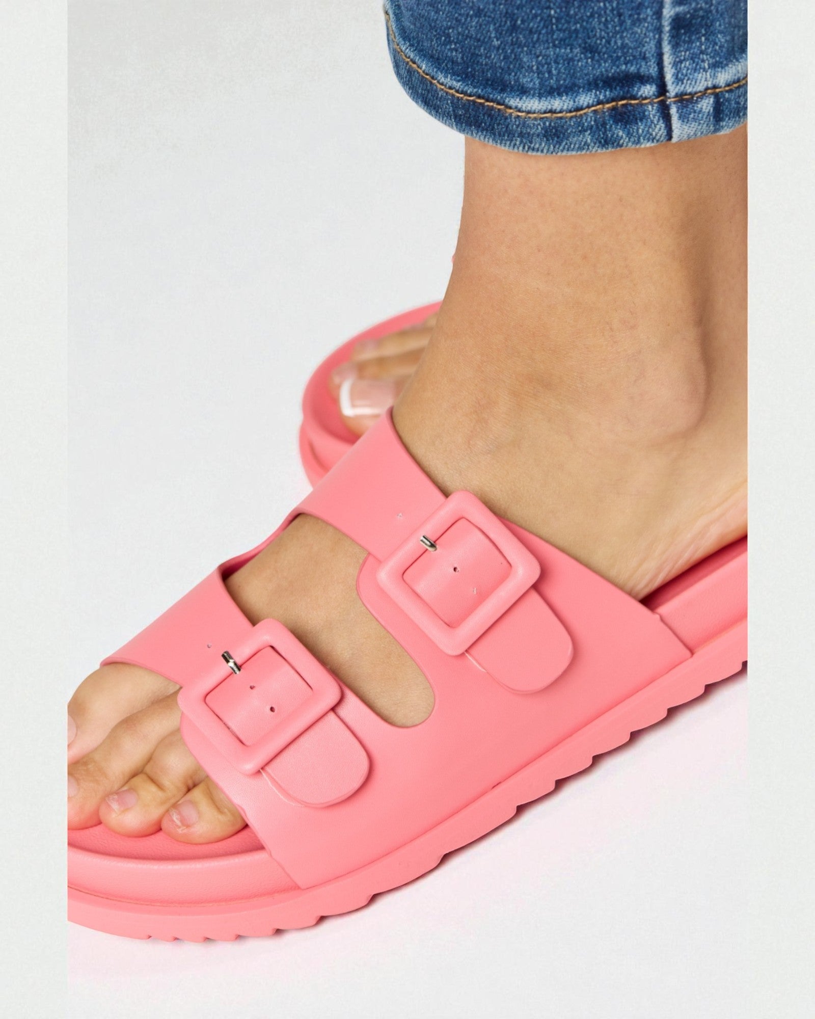 Pink sandals with buckles worn by a person on a white background