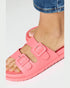 Pink sandals with buckles worn by a person on a white background