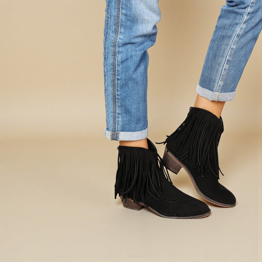 Black fringe boots worn with rolled-up jeans on a beige background