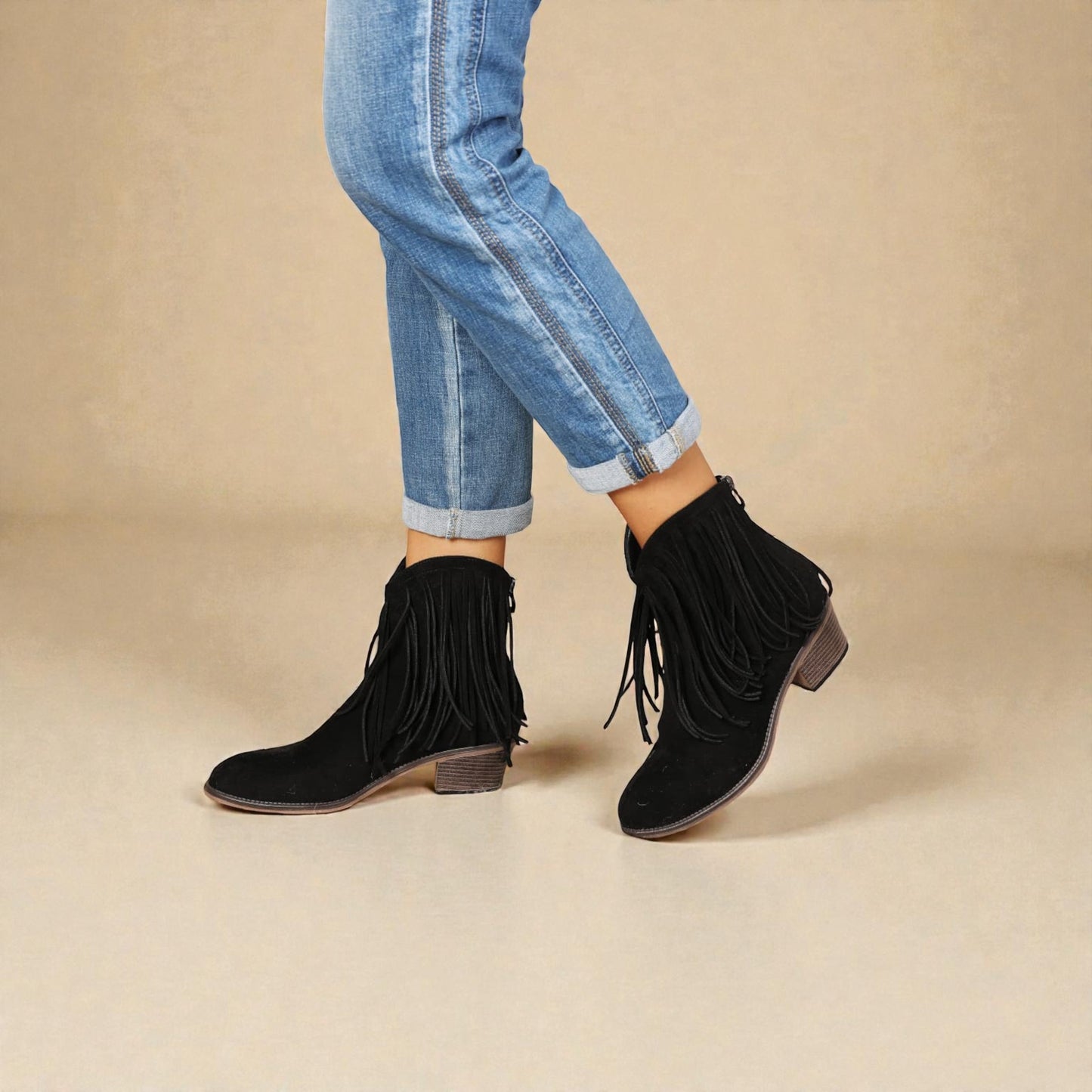 Black fringe ankle boots worn with rolled-up jeans on a beige background