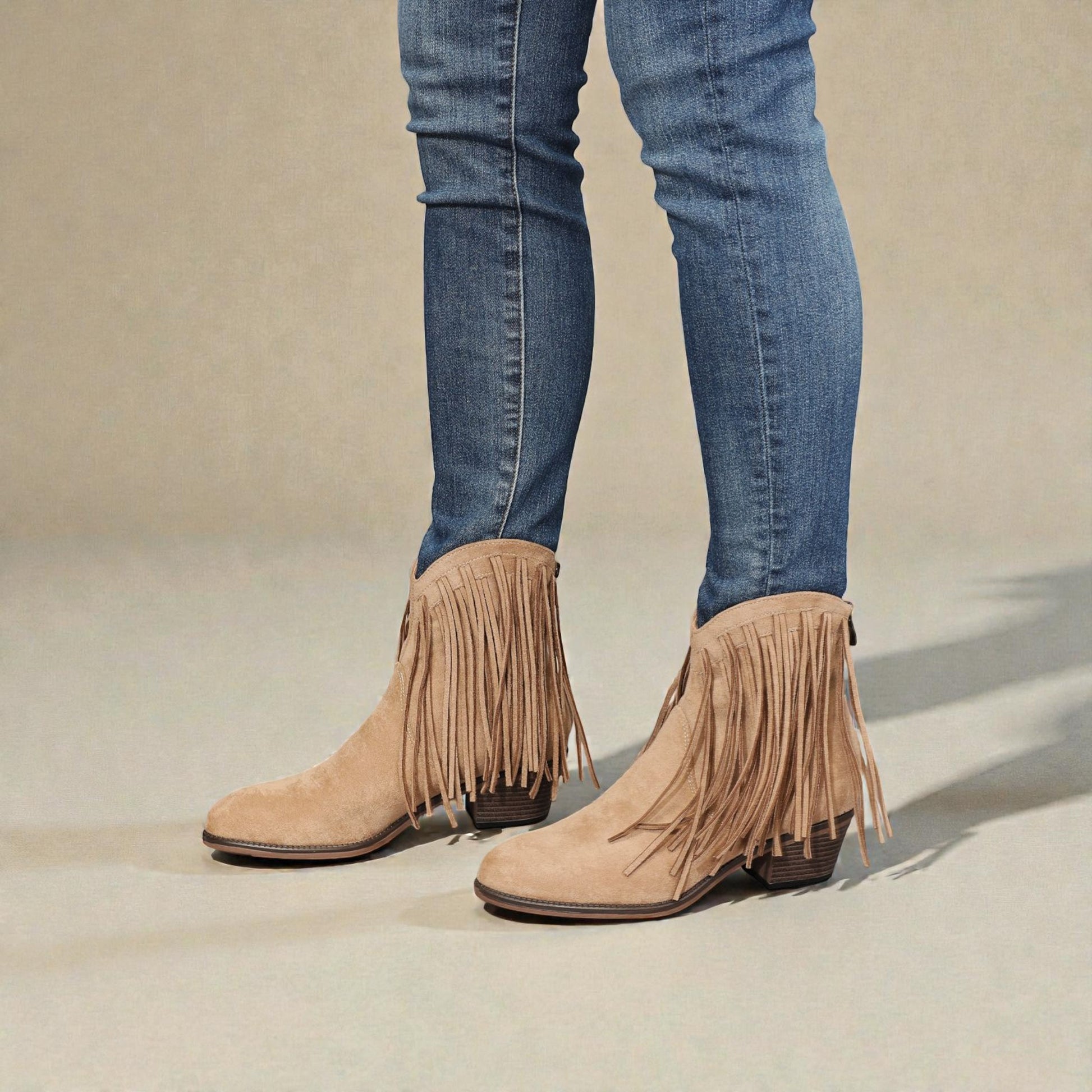 Beige fringe boots worn with blue jeans on a neutral background