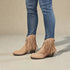 Beige fringe boots worn with blue jeans on a neutral background
